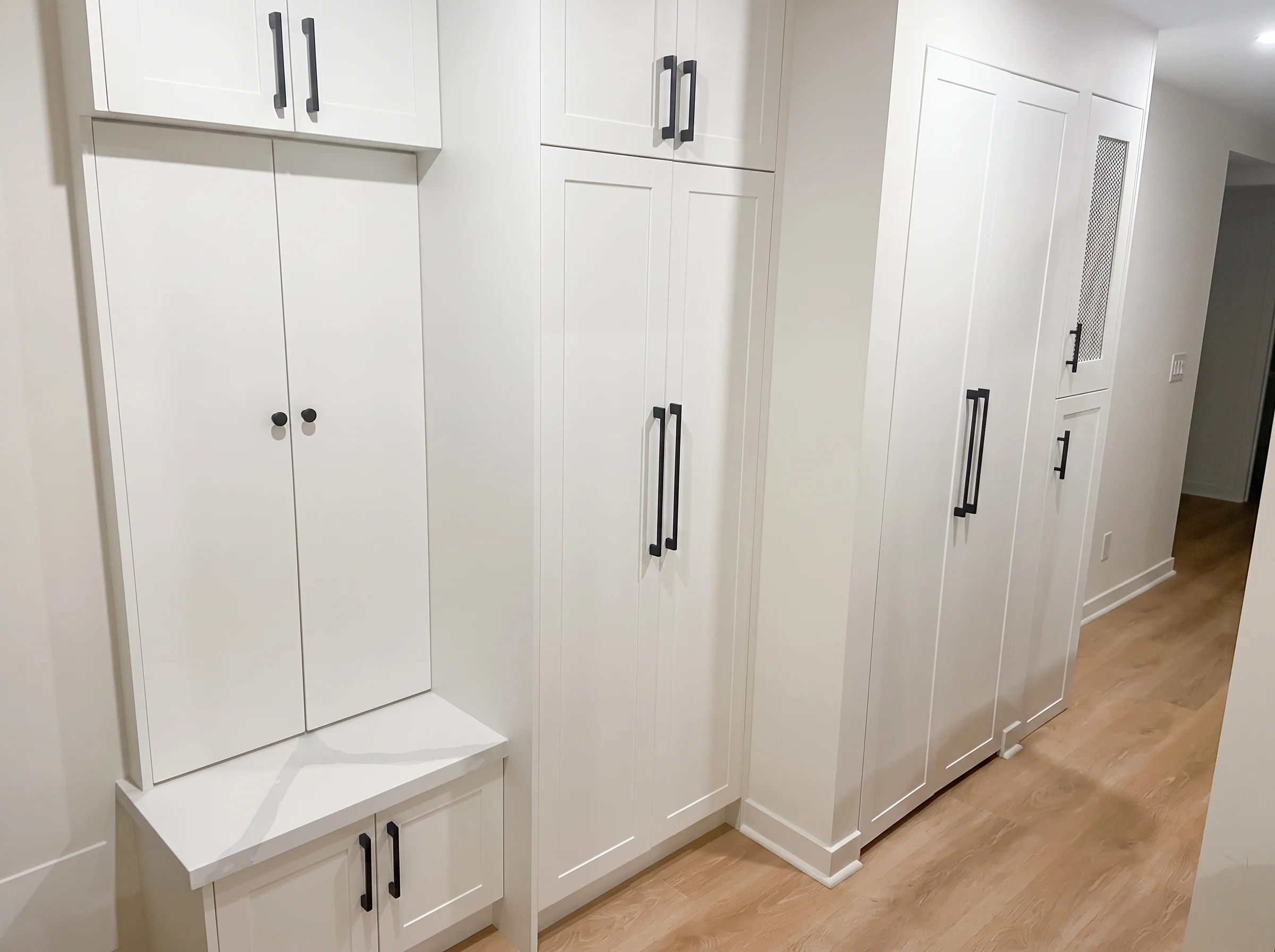 Floor-to-ceiling white shaker built-in pantry and bench run with quartz seat top and matte black pulls