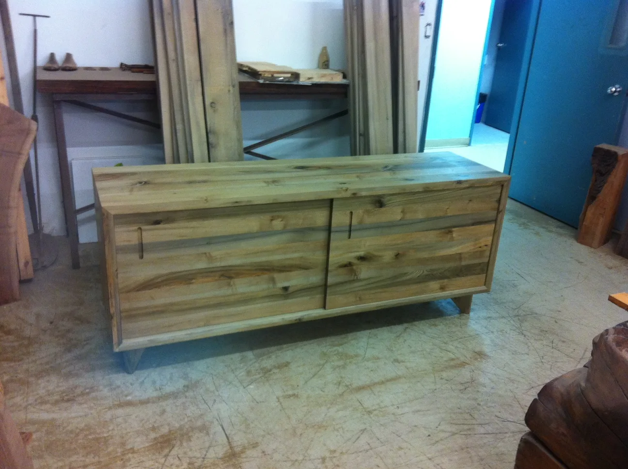 Two-door cabinet built from reclaimed Queen's Wharf lumber, salvaged from Toronto's original harbour cribbing — variegated grain, flush recessed pulls and a tapered plinth base.